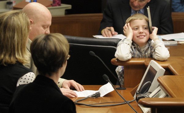 Reece Trahan, 8, who is autistic, rests his arms on the podium as his father, Brad, left top, and mother, Joanie, left center, founders of the Autism Awareness Foundation, Inc., testify Feb. 24 before the House Commerce and Labor Committee in support of a bill that would require insurance carriers to cover autism spectrum disorders. Rep. Kim Norton, left bottom, sponsors HF359. (Photo by Tom Olmscheid)