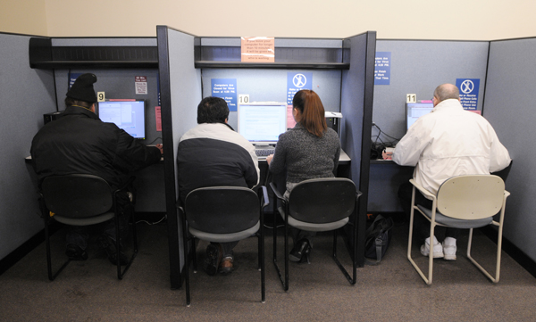 A workforce employee assists a client with filling out a claim, while other clients search job postings on computers at a Workforce Center in St. Paul.
