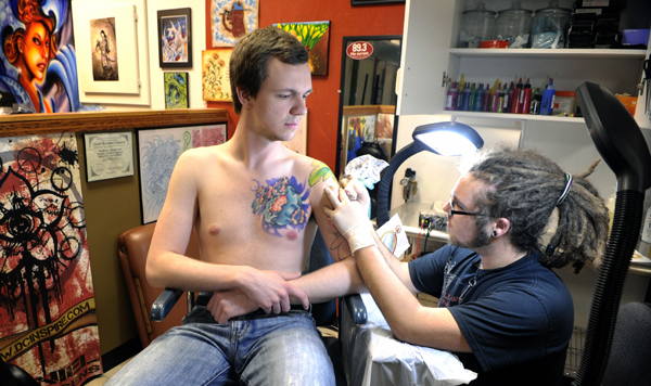Tattoo artist Dan Claessens works on a new tattoo on the shoulder and arm of Corwin Johnson during an April 13 session at Beloved Studios in St. Paul. (Photo by Tom Olmscheid)