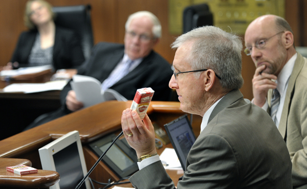 Holding a pack of  what is known as �little cigars,� Thomas Briant, executive director of the Minnesota Wholesale Marketers Association, tells the House Taxes Committee April 28 that a bill to change excise taxation and the regulation of tobacco products could cost the state revenue. Rep. Jim Davnie, right, sponsors the bill. Listening to the testimony are Rep. Debra Hilstrom and Rep. Loren Solberg. (Photo by Tom Olmscheid)