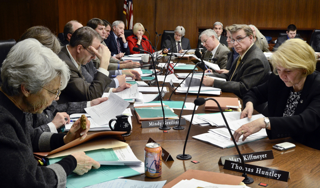 Members of the House Ways and Means Committee wade through bill copies and amendments on the committee table during the March 23 hearing. (Photo by Andrew VonBank)